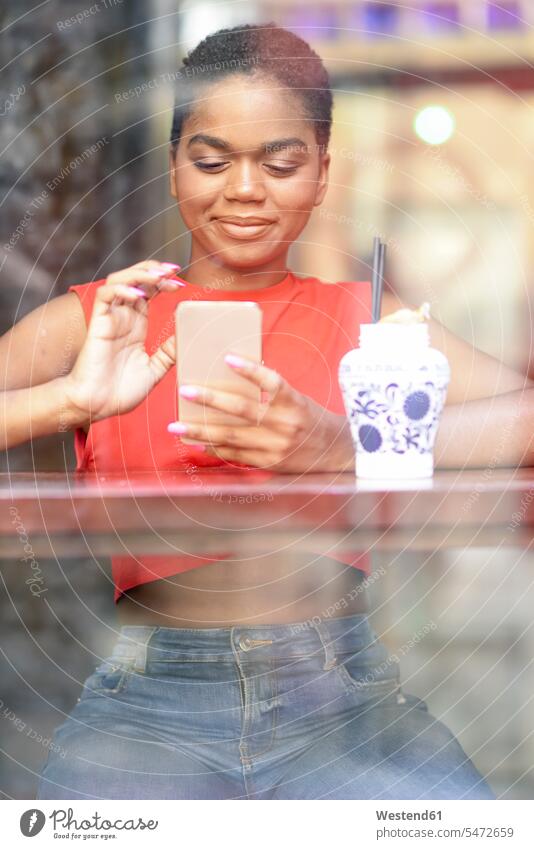 Porträt einer lächelnden jungen Frau in einer Bar, die auf ein Mobiltelefon schaut Leute Menschen People Person Personen Afrikanisch Afrikanische Abstammung