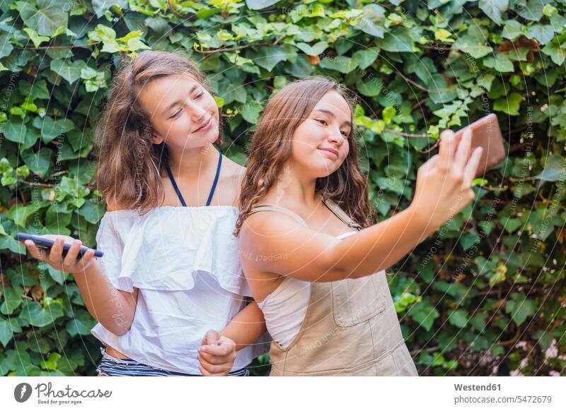 Junge Mädchen nehmen ein Selfie auf Efeu Hintergrund Freunde Kameradschaft Freundin Hecken entspannen relaxen Jahreszeiten sommerlich Sommerzeit entspanntheit