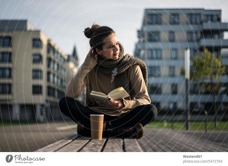 Melancholische Frau mit Kaffee zum Mitnehmen und Buch sitzen auf Bank im Herbst Bücher weiblich Frauen sitzend sitzt Melancholie Schwermut melancholisch