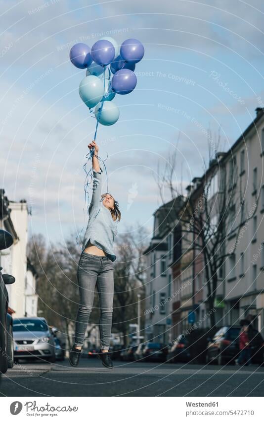 Junge Frau mit blauen Luftballons springt auf der Straße in die Luft Ballons Luftballone blauer blaues Strassen Straßen springen hüpfen weiblich Frauen