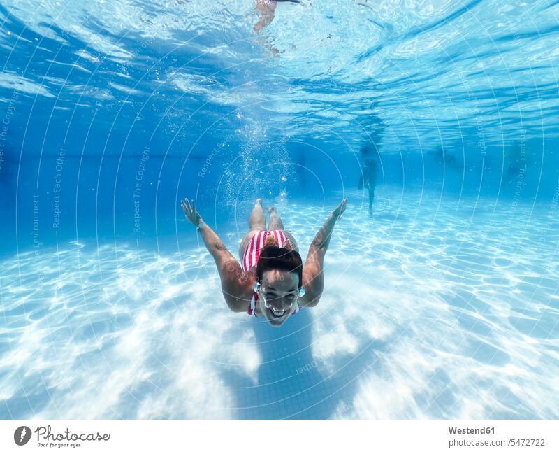 Lächelnde Frau schwimmt unter Wasser im Pool eines Touristenortes Farbaufnahme Farbe Farbfoto Farbphoto Tag Tageslichtaufnahme Tageslichtaufnahmen Tagesaufnahme
