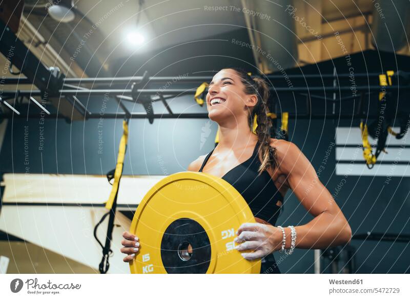 Lächelnde Frau trainiert mit einem Gewicht in einem Fitnessstudio fit gesund Gesundheit Fitnessgeraet Fitnessgeraete Fitnessgeräte Gewichte ausüben trainieren