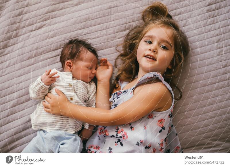 Lächelndes Mädchen liegt auf Decke kuscheln mit ihrem kleinen Bruder Baby Babies Babys Säuglinge Kind Kinder Decken lächeln schmusen knuddeln weiblich liegen