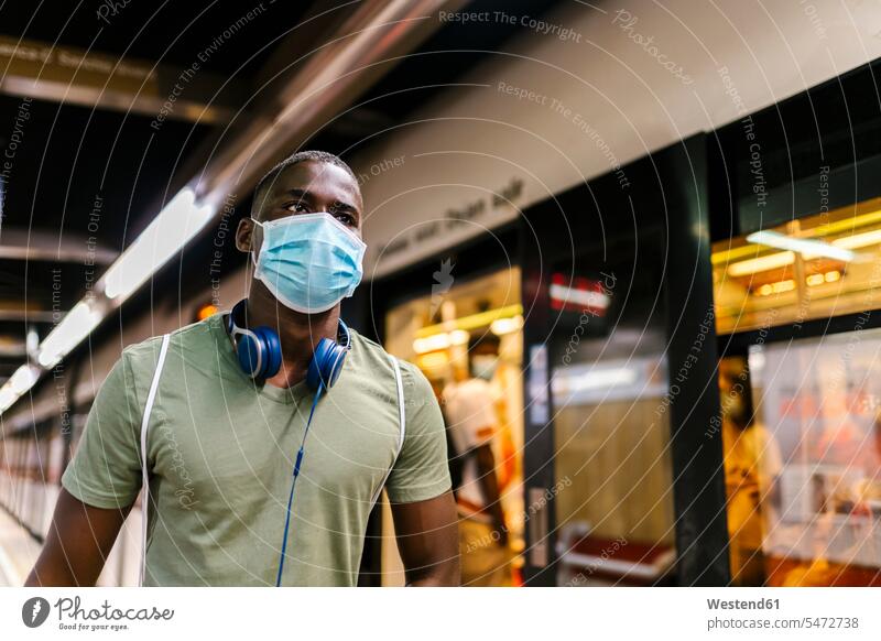 Junger Mann mit Maske schaut weg, während er in der U-Bahn-Station steht Farbaufnahme Farbe Farbfoto Farbphoto Spanien Freizeitkleidung Freizeitbekleidung