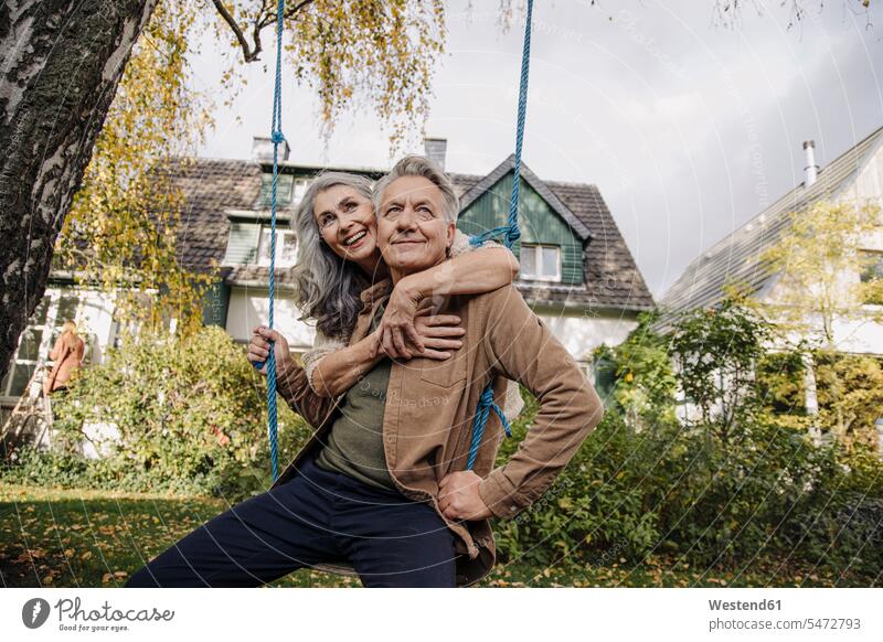 Glückliche Frau umarmt älteren Mann auf einer Schaukel im Garten Schaukeln entspannen relaxen Arm umlegen Umarmung Umarmungen Jahreszeiten entspanntheit relaxt