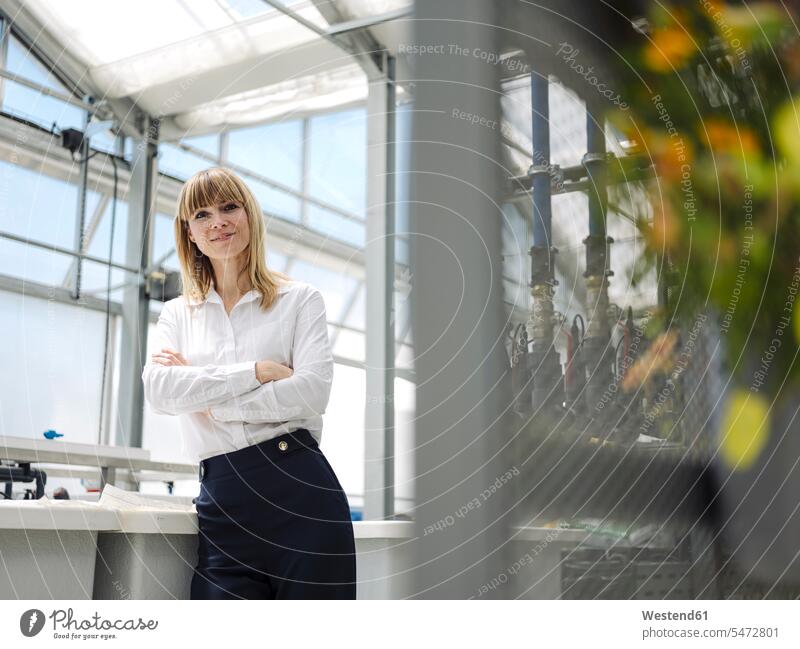 Selbstbewusste Geschäftsfrau mit gekreuzten Armen am Fenster stehend im Gewächshaus Farbaufnahme Farbe Farbfoto Farbphoto Deutschland Geschäftsleute