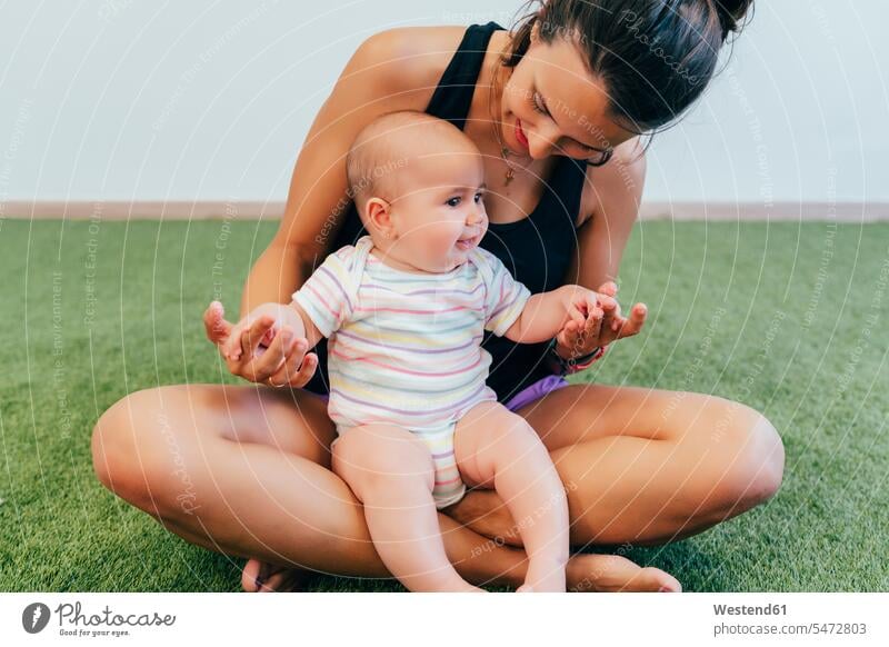 Junge Mutter und Baby beim Mutter-Kind-Turnen trainieren Teppiche sitzend sitzt freuen Frohsinn Fröhlichkeit Heiterkeit geniessen Genuss Glück glücklich sein