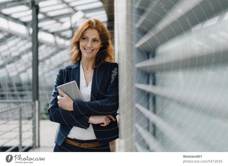 Porträt einer lächelnden Geschäftsfrau, die in einem modernen Bürogebäude ein Tablett hält Job Berufe Berufstätigkeit Beschäftigung Jobs geschäftlich