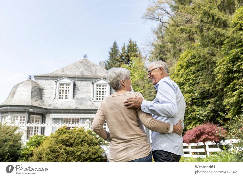Rückansicht eines älteren Ehepaares, das im Garten seines Hauses steht freuen Glück glücklich sein glücklichsein zufrieden stehend daheim zu Hause Pension