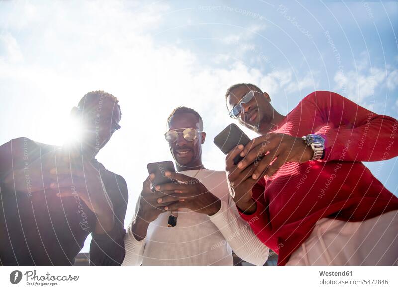 Drei coole junge Männer mit Mobiltelefonen im Gegenlicht Leute Menschen People Person Personen Afrikanisch Afrikanische Abstammung dunkelhäutig Farbige Farbiger