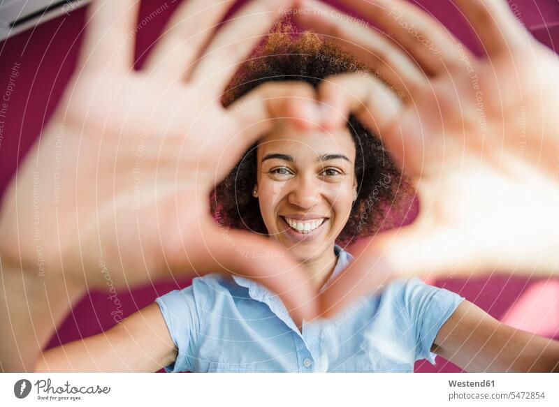 Lachende junge Frau, die durch einen herzförmigen Fingerrahmen schaut Job Berufe Berufstätigkeit Beschäftigung Jobs freuen Glück glücklich sein glücklichsein