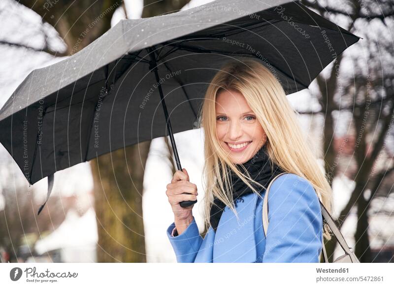 Porträt einer lächelnden blonden Frau, die einen Regenschirm im Freien hält Schals Schirme Regenschirme freuen Glück glücklich sein glücklichsein zufrieden
