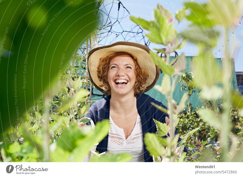 Porträt einer glücklichen jungen Frau mit Stroh im Stadtgarten Glück glücklich sein glücklichsein weiblich Frauen Strohhut Strohhüte Strohhuete Portrait