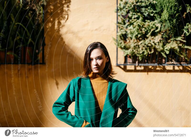 Schöne Frau in grüner Jacke steht an sonnigen Tagen gegen Gebäude in der Stadt Farbaufnahme Farbe Farbfoto Farbphoto Spanien Freizeitkleidung Freizeitbekleidung