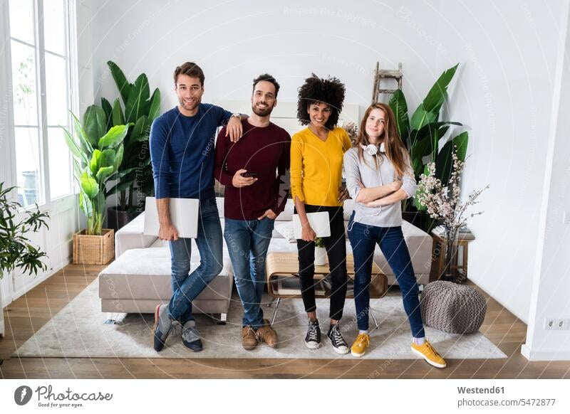 Porträt von vier glücklichen Freunden, die Seite an Seite im Wohnzimmer stehen Leute Menschen People Person Personen Europäisch Kaukasier kaukasisch Afrikanisch