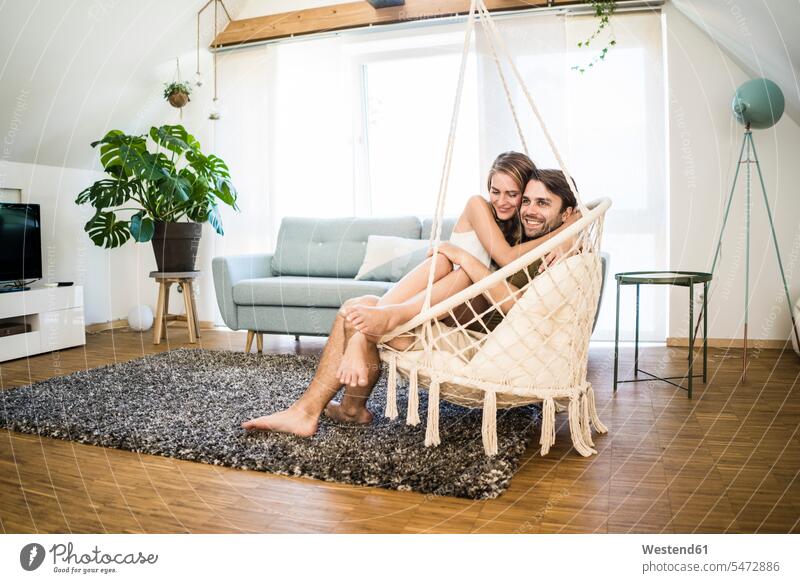 Glückliches liebevolles Paar sitzt in Hängesessel zu Hause Zuneigung sitzen sitzend glücklich glücklich sein glücklichsein Zuhause daheim Pärchen Paare