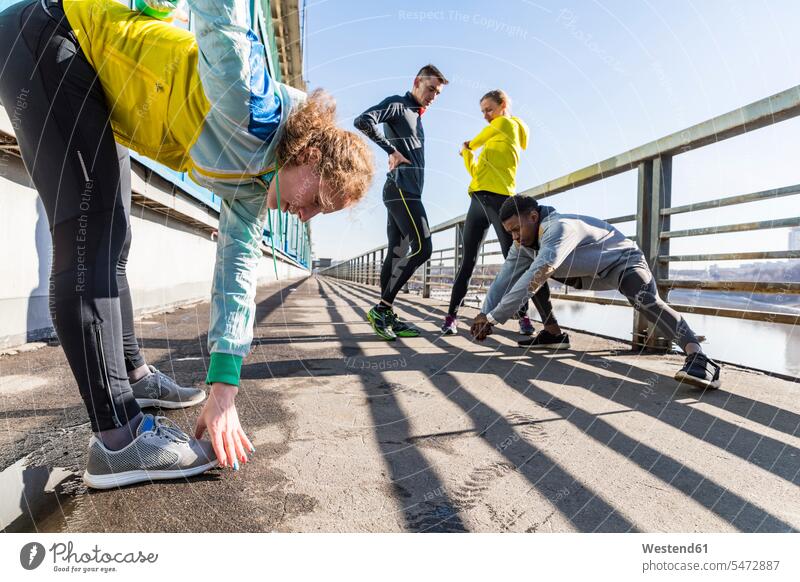 Freunde machen Dehnungsübung auf der Brücke in der Stadt Übung Uebung Übungen Uebungen staedtisch städtisch dehnen strecken Außenaufnahme draußen im Freien