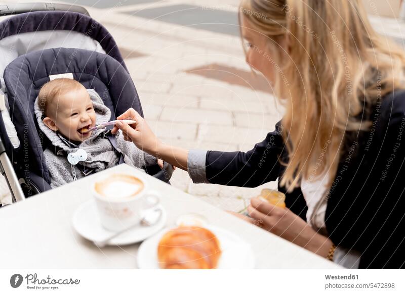 Mutter füttert lachendes Baby Junge im Kinderwagen essen essend Löffel Gebäck Backware Gebaeck Backwaren Spaß Spass Späße spassig Spässe spaßig niedlich süss