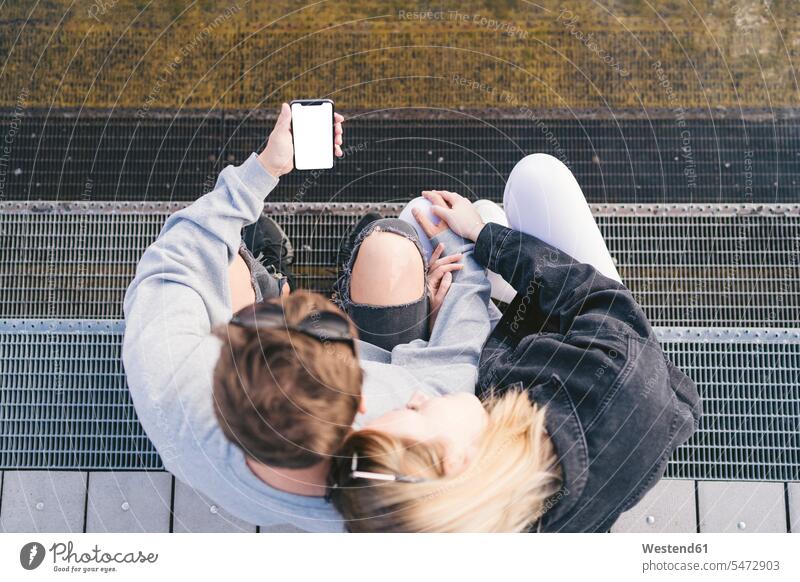 Junges Paar sitzt auf der Treppe und schaut auf das Smartphone Informationen Telekommunikation Handies Handys Mobiltelefon Mobiltelefone Displays Lektüre