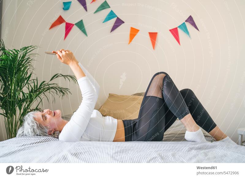 Glückliche Frau auf dem Bett liegend zu Hause ein Selfie machen Leute Menschen People Person Personen Alleinstehende Alleinstehender Singles Unverheiratete