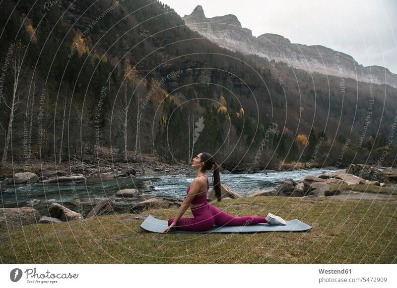 Aktive Frau praktiziert Yoga auf der Matte am Fluss und in den Bergen im Ordesa-Nationalpark, Huesca, Spanien Farbaufnahme Farbe Farbfoto Farbphoto