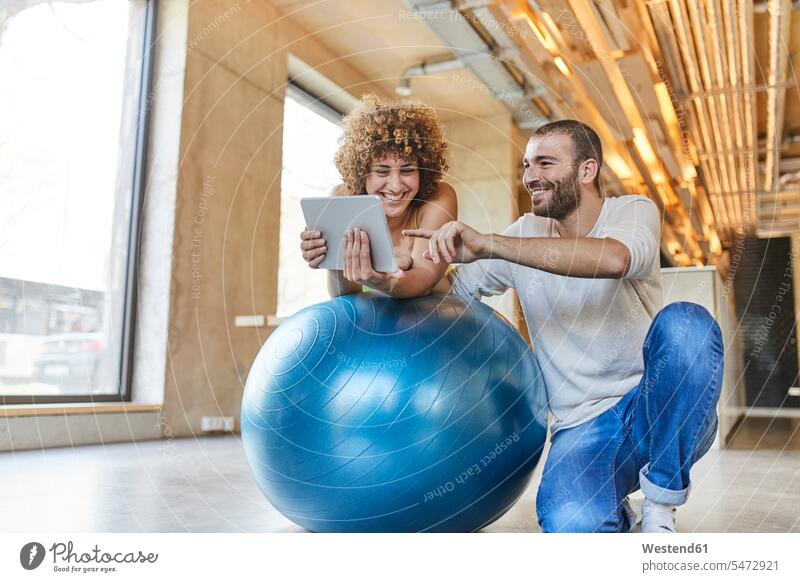 Glücklicher Mann und Frau mit Tablette auf Fitness-Ball in modernen Büro Deutschland Achtsamkeit bewusst Bewusstheit achtsam Fitnessball Gymnastikball Sitzball