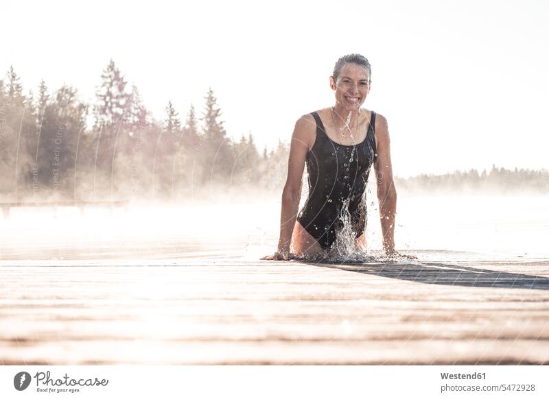 Glückliche Frau im schwarzen Badeanzug badet im Morgennebel in einem See Badebekleidung Badeanzuege Badeanzüge früh Frühe entspannen relaxen entspanntheit