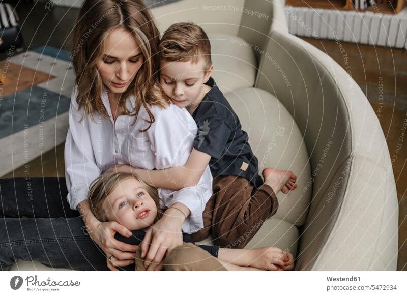 Blonde Frau sitzt mit Söhnen auf dem Sofa im Wohnzimmer zu Hause Farbaufnahme Farbe Farbfoto Farbphoto Innenaufnahme Innenaufnahmen innen drinnen