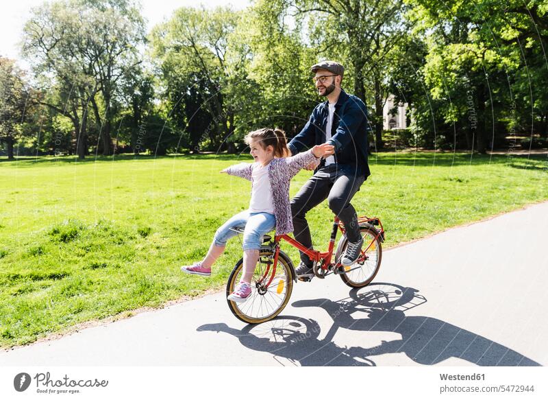Glücklicher Vater fährt Fahrrad mit Tochter in einem Park Bikes Fahrräder Räder Rad radfahren fahrradfahren radeln aktiv Töchter Parkanlagen Parks Papas Väter