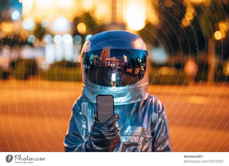 Spaceman auf einer Straße in der Stadt in der Nacht hält Smartphone staedtisch städtisch Handy Mobiltelefon Handies Handys Mobiltelefone Astronaut Astronauten