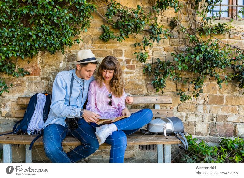 Junges Paar auf einer Städtereise, auf einer Bank sitzend, Reiseführer lesend Tourist Touristen Gemeinsamkeit zusammen gemeinsam Steinmauer Steinmauern