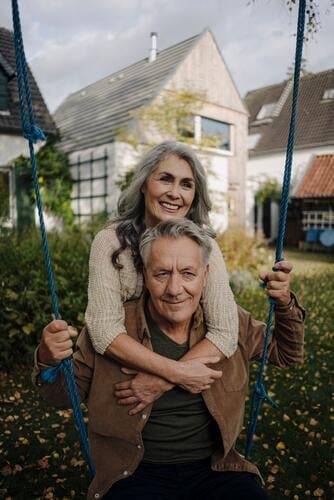 Glückliche Frau umarmt älteren Mann auf einer Schaukel im Garten Leute Menschen People Person Personen Europäisch Kaukasier kaukasisch 2 2 Menschen 2 Personen