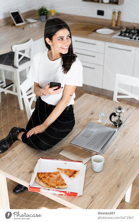 Junge Frau mit Handy essen Pizza in der Küche zu Hause Leute Menschen People Person Personen Alleinstehende Alleinstehender Singles Unverheiratete