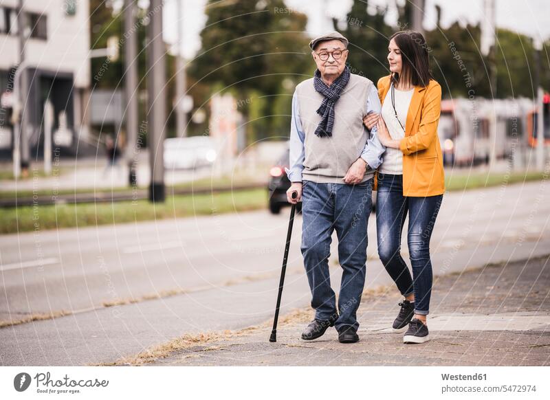 Erwachsene Enkelin hilft ihrem Großvater beim Spaziergang mit einem Spazierstock Generation gehend geht Muße Miteinander Zusammen Lifestyles außen draußen