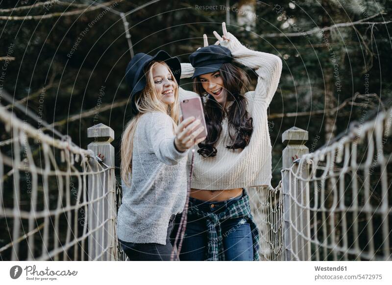 Zwei glückliche junge Frauen auf einer Hängebrücke machen ein Selfie Haengebruecke Hängebrücken Haengebruecken Glück glücklich sein glücklichsein weiblich