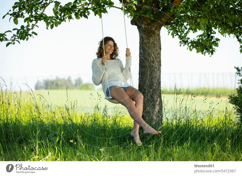 Lächelnde junge Frau auf der Schaukel sitzend sitzt Sommer Sommerzeit sommerlich Leichtigkeit leicht schaukeln schwingen Schaukeln Freizeit Muße weiblich Frauen