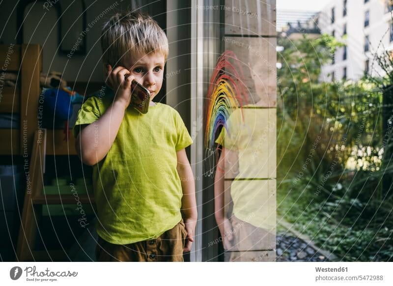 Porträt eines kleinen Jungen am Telefon zu Hause Fensterscheiben T-Shirts Telekommunikation telefonieren Handies Handys Mobiltelefon Mobiltelefone hoeren Anruf