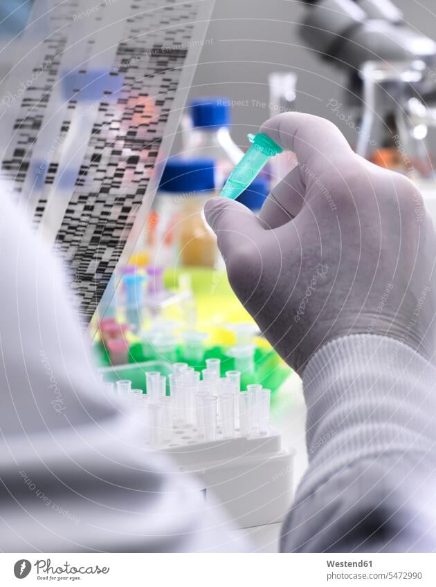 Wissenschaftlerin hält ein DNA-Gel in der Hand, das die genetische Zusammensetzung der Probe im Fläschchen offenbart Experiment experimentieren Genforschung