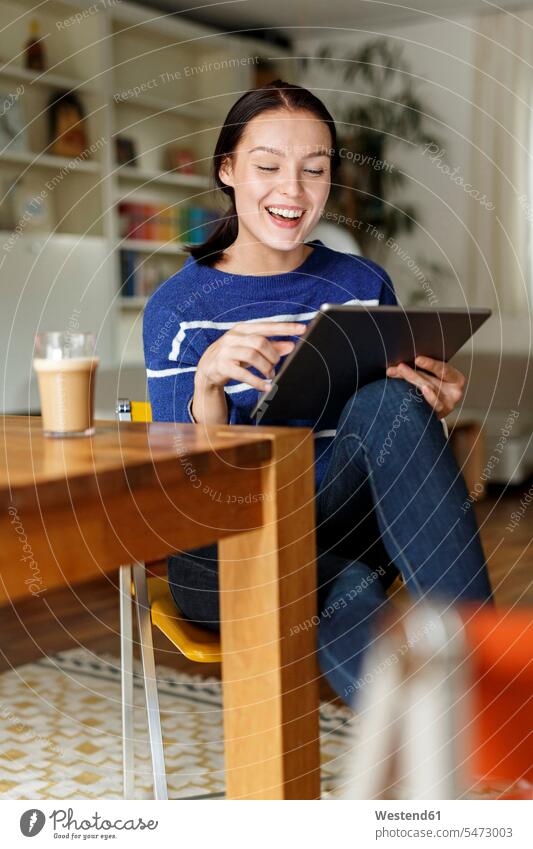 Junge Frau sitzt zu Hause und benutzt ein digitales Tablet Smart Home smarthome lachen benutzen benützen betrachten betrachtend Zuhause daheim junge Frau