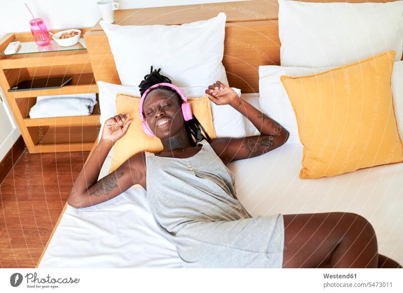 Frau hört Musik über Kopfhörer, während sie sich zu Hause im Bett entspannt Farbaufnahme Farbe Farbfoto Farbphoto Innenaufnahme Innenaufnahmen innen drinnen