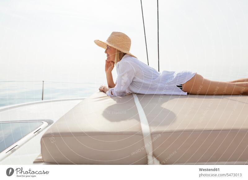 Reife Frau entspannt sich auf einem Katamaran und nimmt ein Sonnenbad reife Frau reife Frauen Schiffsdeck Decks Schiffsdecks sonnenbaden sich sonnen Matratze