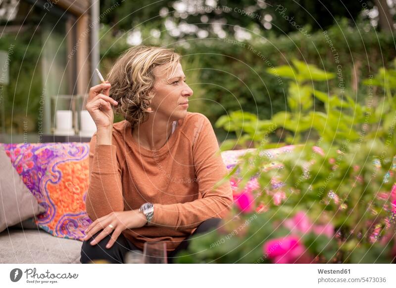 Frau hält Zigarette in der Hand, während sie auf dem Sofa im Hinterhof sitzt Farbaufnahme Farbe Farbfoto Farbphoto Tag Tageslichtaufnahme Tageslichtaufnahmen