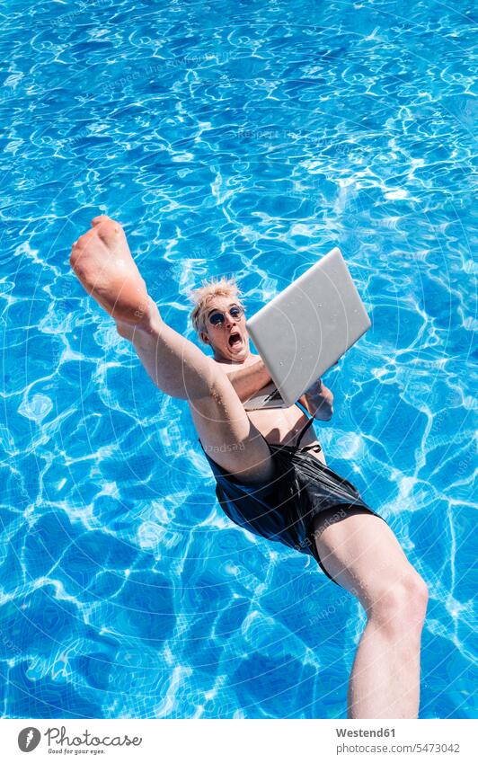 Junger Mann ohne Hemd mit Laptop in der Hand fällt in Schwimmbad Farbaufnahme Farbe Farbfoto Farbphoto Spanien Freizeitbeschäftigung Muße Zeit Zeit haben