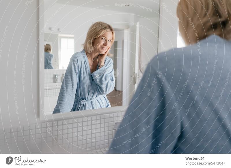 Porträt einer lächelnden reifen Frau, die in den Badezimmerspiegel schaut weiblich Frauen Portrait Porträts Portraits schauen schauend anschauen betrachten