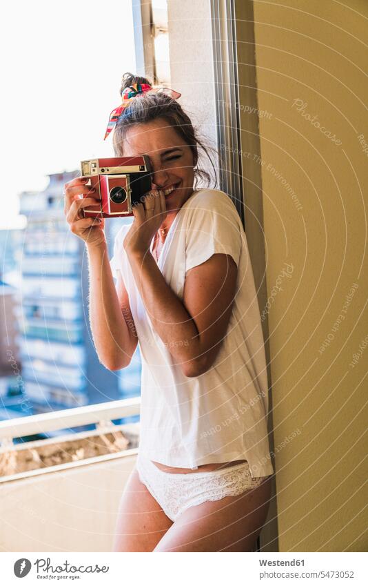 Porträt einer glücklichen jungen Frau, die am Fenster steht und mit einer altmodischen Kamera fotografiert fotografieren T-Shirt T-Shirts Fotograf Fotografen