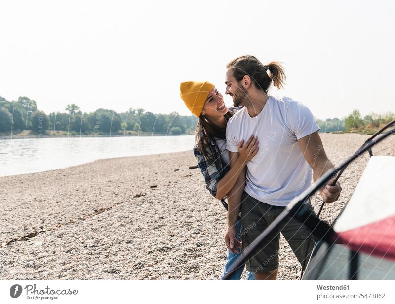 Glückliches junges Paar baut ein Zelt am Flussufer auf aufbauen Zelte glücklich glücklich sein glücklichsein Pärchen Paare Partnerschaft lächeln Ufer Mensch
