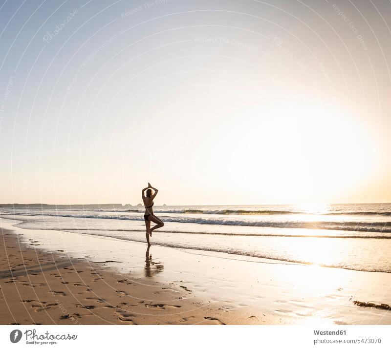 Junge Frau übt Yoga am Strand Meer Meere Yoga-Übungen Yogauebungen Yogaübungen Jogauebung Jogauebungen Baumposition Baumstellung Vrksasana Baum-Stellung