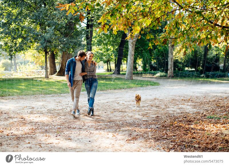 Glückliches junges Paar mit Hund in einem Park Tiere Tierwelt Haustiere Hunde entspannen relaxen gehend geht Arm umlegen Umarmung Umarmungen freuen Frohsinn