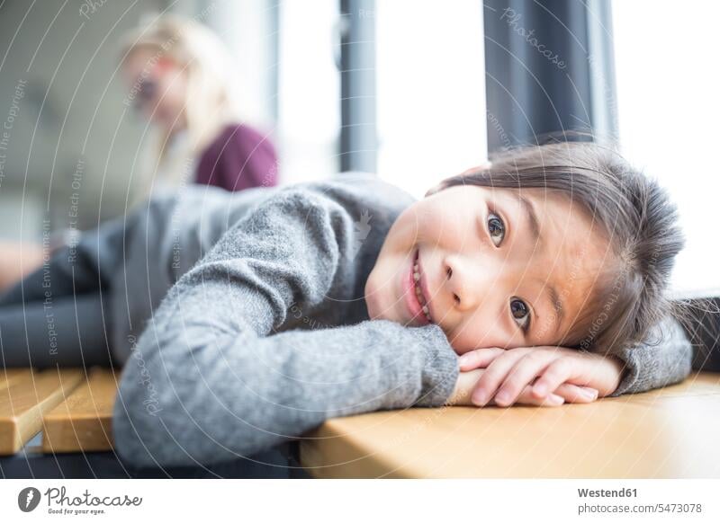 Porträt eines lächelnden Schulmädchens, das in der Schule auf einer Bank liegt liegen Portrait Schülerin Schulkind Bildung Grundschule Entspannung Freude Kind
