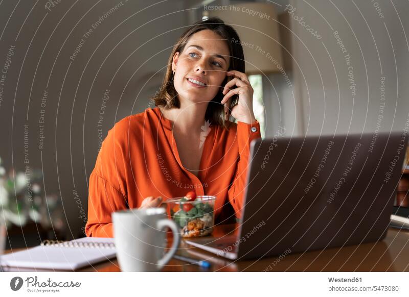 Lächelnde Geschäftsfrau telefoniert mit dem Handy, während sie zu Hause Salat isst Farbaufnahme Farbe Farbfoto Farbphoto Innenaufnahme Innenaufnahmen innen
